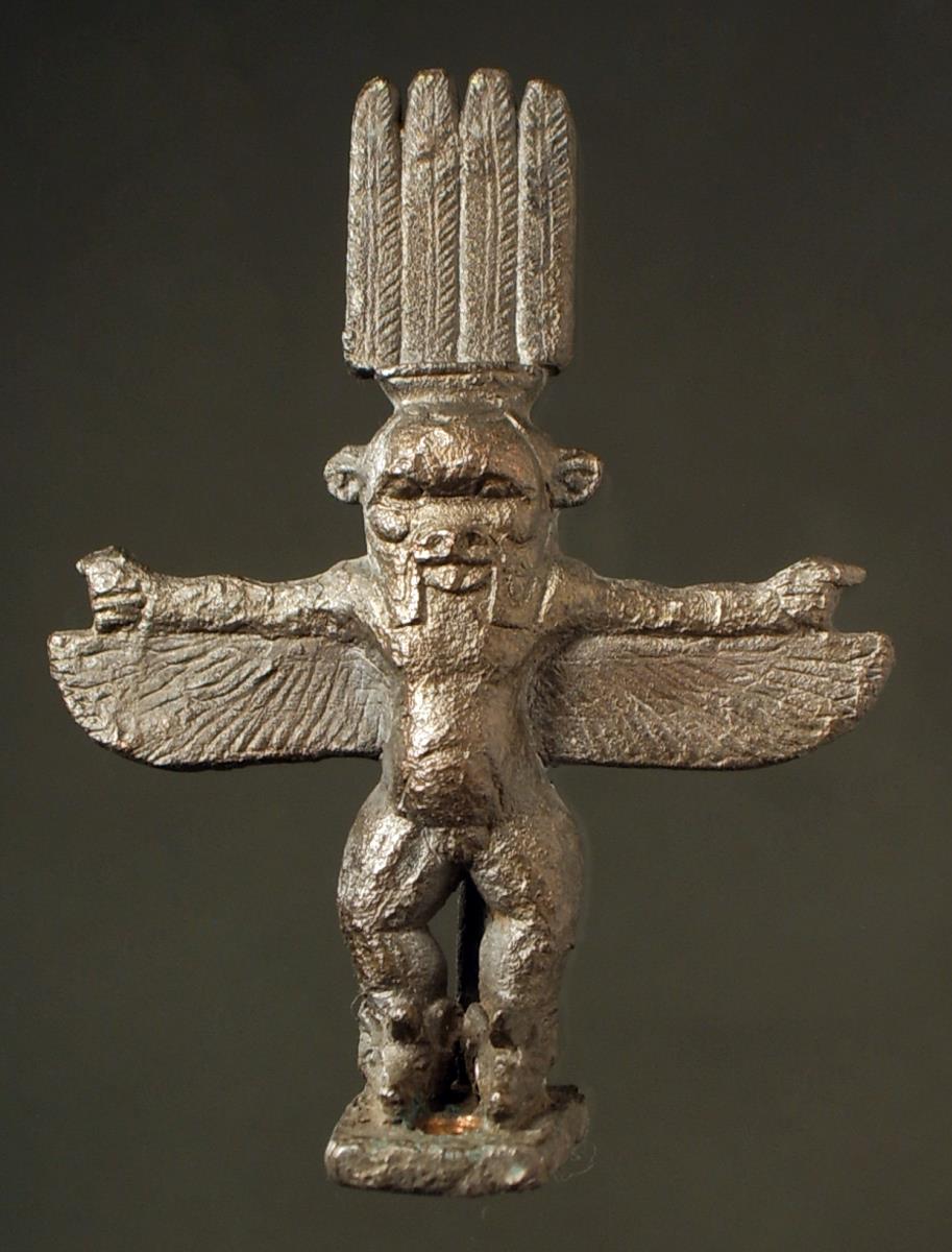 Ägyptische Besstatuette. ""Statuette des geflügelten Bes, der über den gespreizten Flügeln die Arme ausstreckt. Er ist lang gekränzt. Auf dem Haupte eine Art Krone aus 4 Federn.""