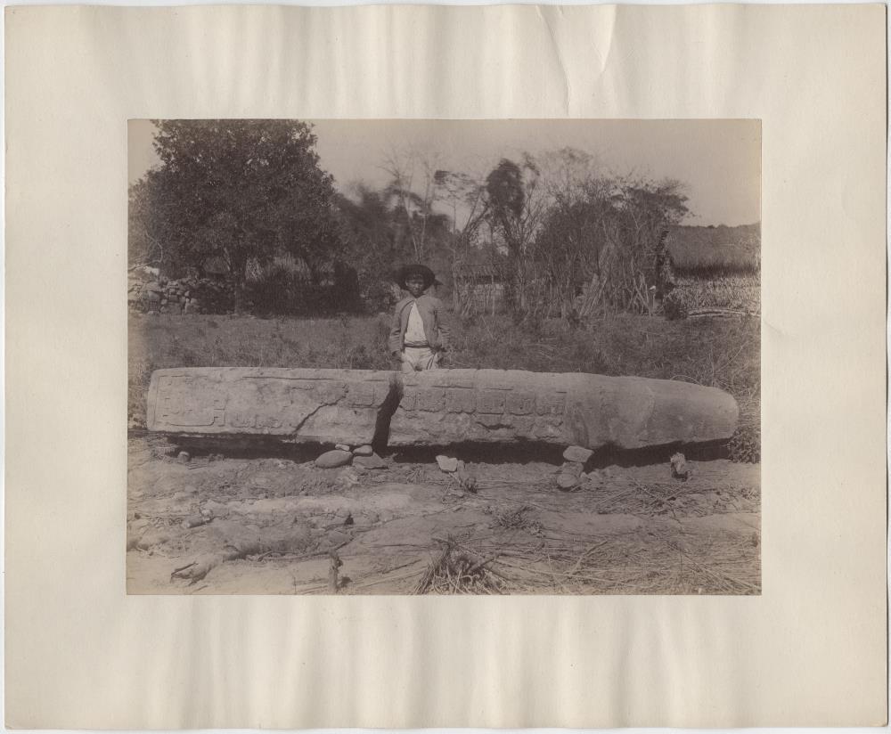 Stele 7, Nordseite. Einheimischer Junge hinter Stele stehend. Dorf Copán im Hintergrund. ("Das gewöhnliche Zeichen der Überschrift")