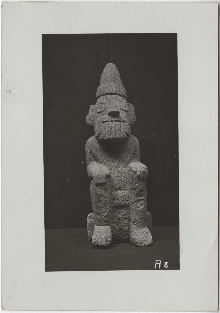 Hockende Tlaloc-Figur aus hellgrauem Kalkstein mit der charakteristischen spitzen Mütze des Frühlingsgottes Xipe ("Fruchtbarkeit als Folge des Regens). Höhe: 37 cm." (B.T)