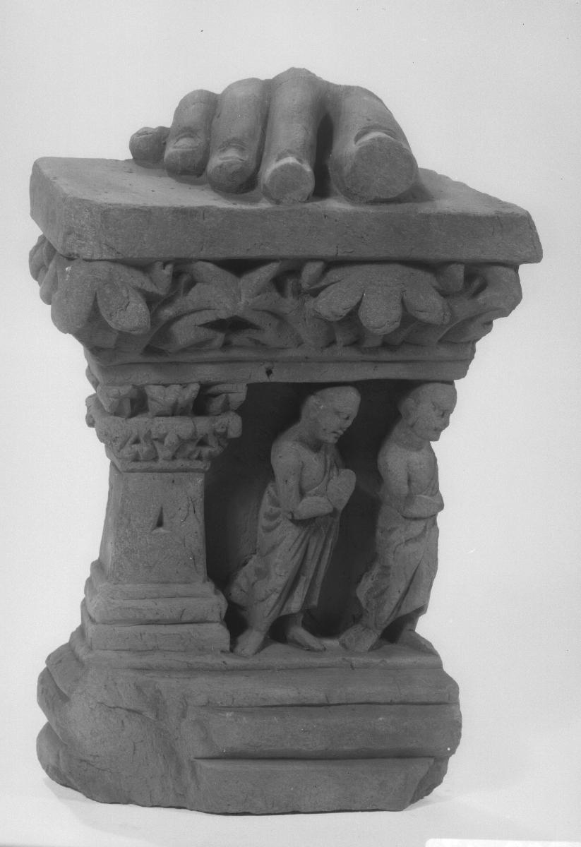 Fuß eines stehenden Buddha (Fragment). Sockelrelief: zwei Mönche unter Akanthusblattfries