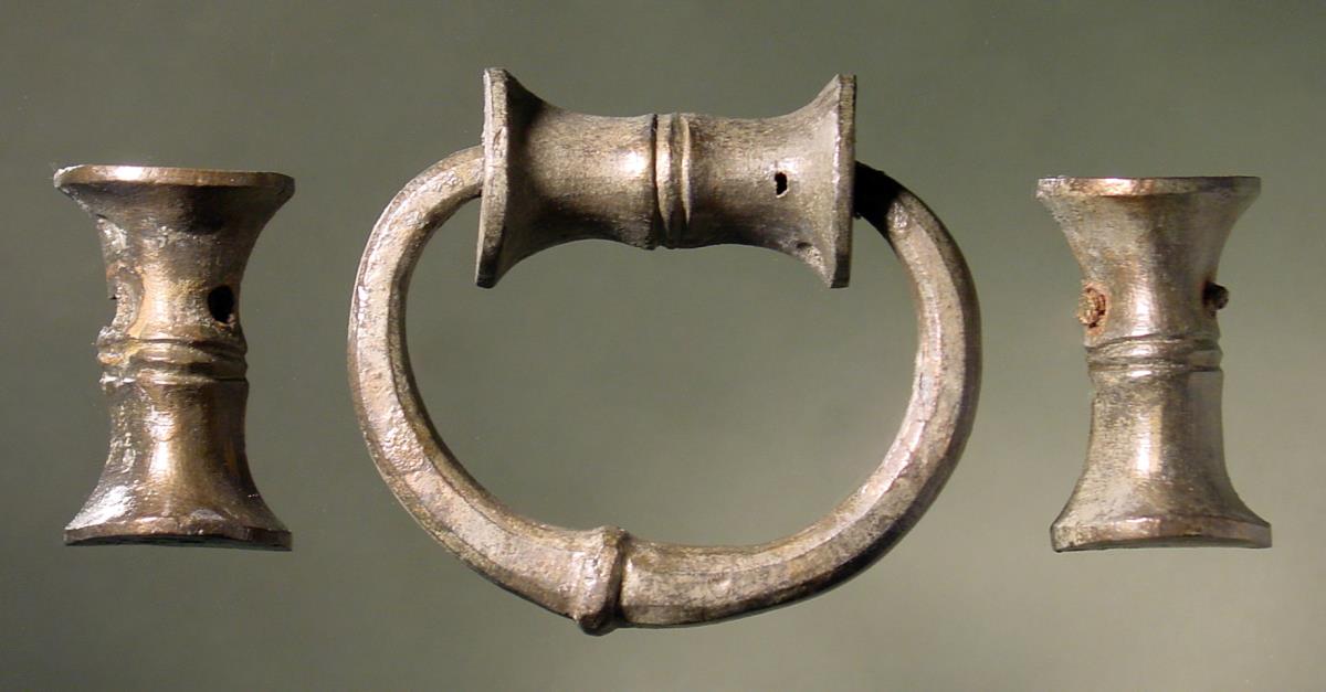 Ovaler Henkel oder Griff mit einem Einsatzstück, vorne rund, hinten glatt, und zwei (Rotellen)