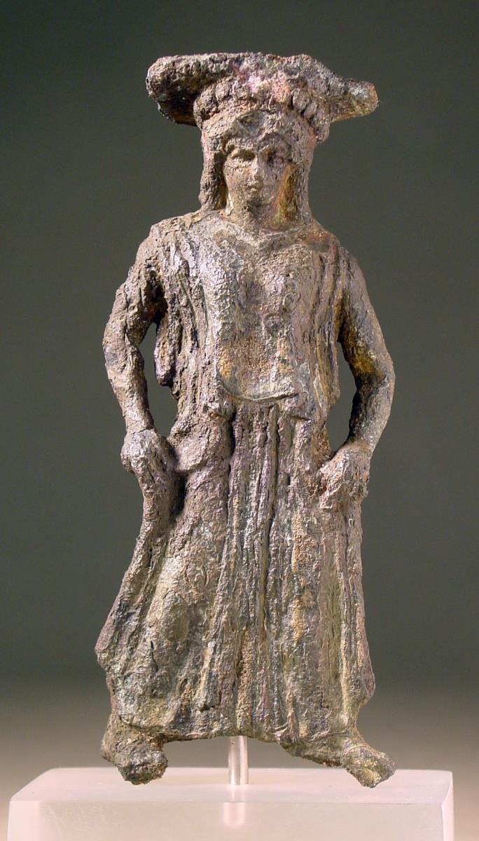 "Spiegelgriff. Weibliche Figur in langem Gewande nach R bewegt, Gesicht en face, mit beiden Händen das Gewand hebend, auf einem ionischen Kapitell (0,11 hoch), durch Oxydation sehr entstellt" (eher frühklassische Stützfigur eines Perirrhanterions)