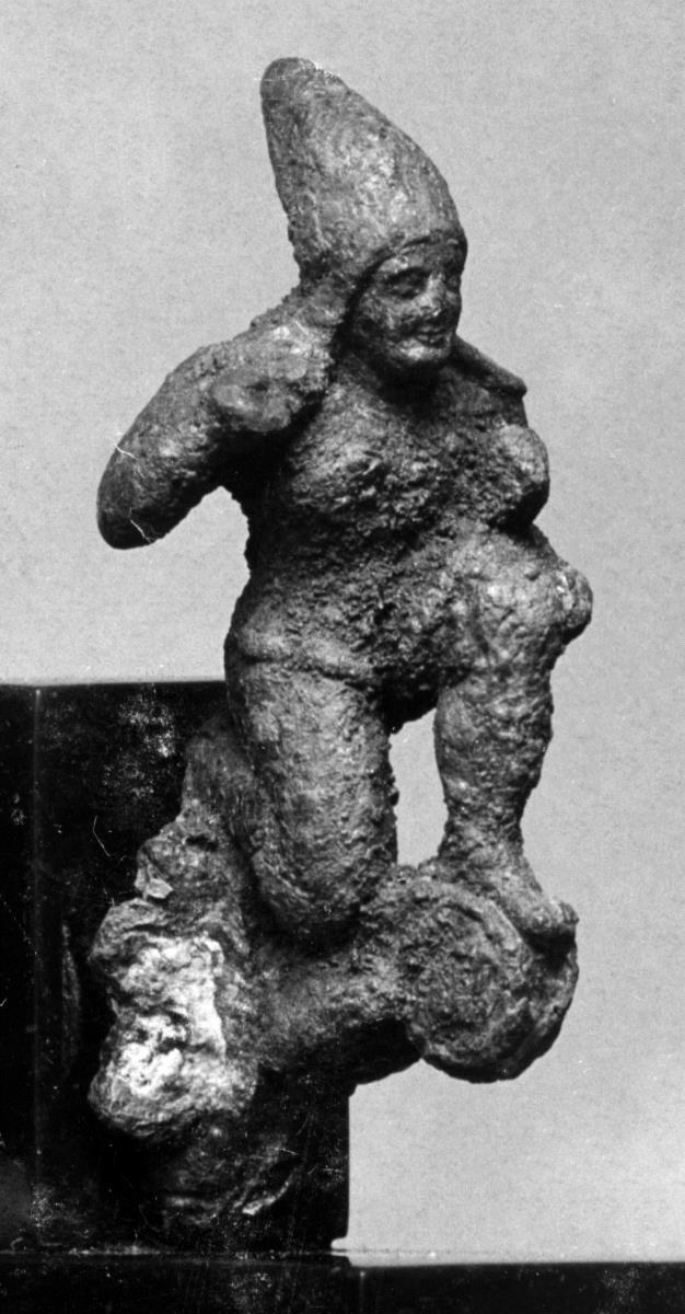 Applik eines etruskischen Helms: Kleines Figurchen eines unbärtigen, knienden Bogenschützen mit hohem, spitzen Helm; auf einer Volute