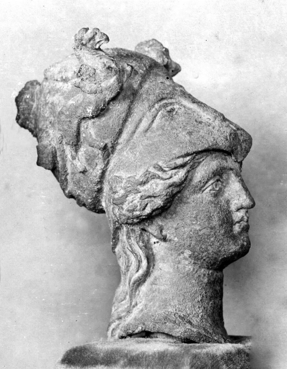 Athenakopf mit korinthischem Helm, daran zwei Greifen im Relief; Helmbusch abgebrochen; Helmspitze vorne eingedrückt
