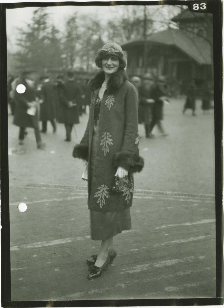 Frau in Kleid und Mantel auf dem Rennplatz