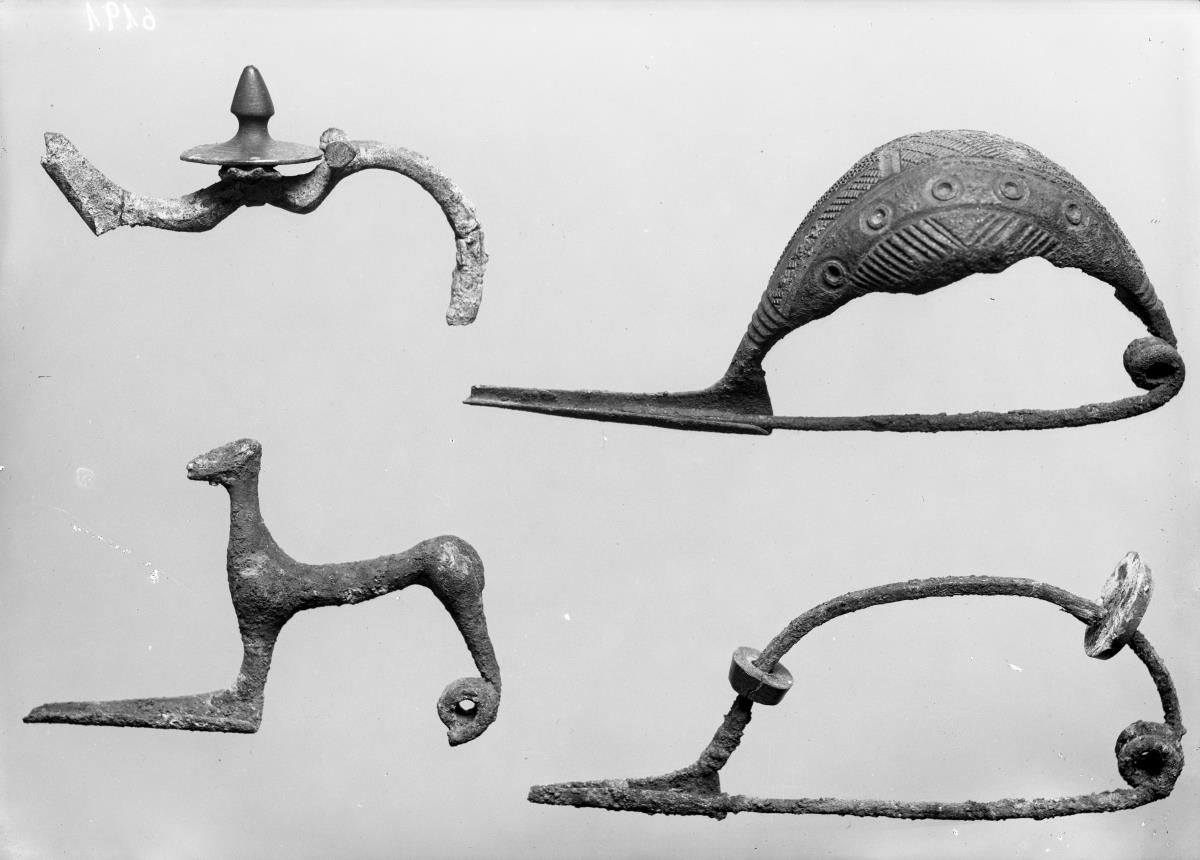 Lange feine Fibel; gut erhalten. Der Bügel war mit Holzscheiben und Bernsteinscheiben bekleidet; von den Holzscheiben sind drei, von den Bernsteinscheiben eine erhalten; außerdem ist noch eine Scheibe aus Knochen erhalten