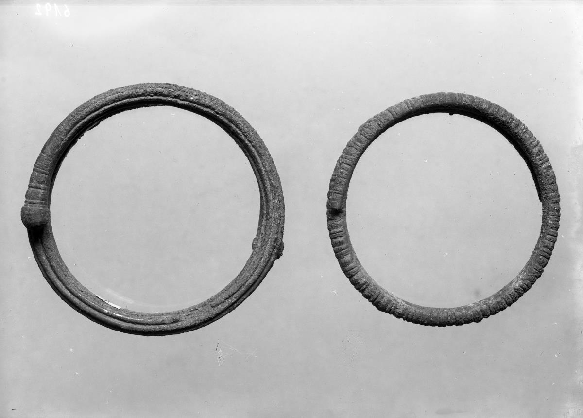 Massiver runder Armring von rundem Querschnitt mit übergreifenden Enden; an der Außenseite mit sechs kannelurenartigen Rillen; an den Enden mit runden Knöpfen versehen, vor welchen halbumlaufende Einkerbungen