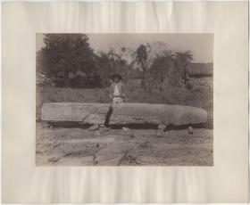 Stele 7, Nordseite. Einheimischer Junge hinter Stele stehend. Dorf Copán im Hintergrund. ("Das gewöhnliche Zeichen der Überschrift")
