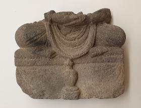 Unterkörper eines meditierenden Buddha oder zukünftigen Buddha Maitreya auf Thron mit Vorhangmotiv (Fragment). Sockelrelief: Flasche (kamandalu)