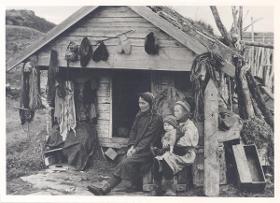 Samin mit zwei Kindern vor Holzhaus