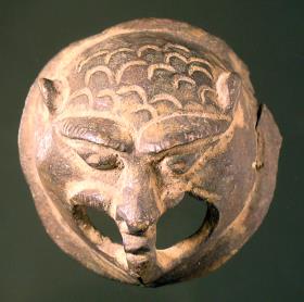 Runde, stilisierte Löwenmaske mit doppelt durchbohrtem Maul