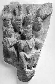 Acht stehende Adoranten (drei fragmentarisch), vier mit Turban,  einer mit Haarknoten/Ushnisha, scharen sich um einen sitzenden, ranghohen Turbanträger mit Lotosblüte (Fragment)