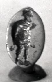 Fingerring aus goldiger Bronze. Auf der Abplattung die Figur eines dickbäuchigen Mannes (Schauspieler?)