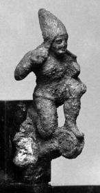 Applik eines etruskischen Helms: Kleines Figurchen eines unbärtigen, knienden Bogenschützen mit hohem, spitzen Helm; auf einer Volute