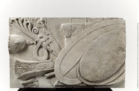 Brüstungsrelief (Waffenrelief) der Hallen des Athenaheiligtums in Pergamon. Linker Teil einer vollständigen, aus zwei Teilen bestehenden Brüstungsplatte: zwei Schilde vor größerem ovalen (gallischen) Schild; dahinter ein Panzer mit pflanzlichem und geometrischem Dekor, ein Langschwert und ein Helm sowie ein Steuerruder, mit pflanzlichem Dekor und einem Seeungeheuer verziert