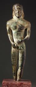 Archaische Statuette eines bärtigen Mannes, bis auf die Füße wohl erhalten. Beide Hände zusammen vor dem Unterleib, beide durchbohrt, Nase abgestoßen
