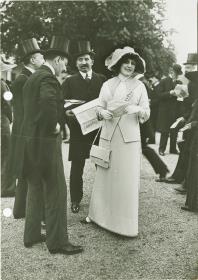 Frau in Ensemble und Männer in Anzügen auf dem Rennplatz