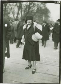 Frau in Kleid und Mantel auf dem Rennplatz