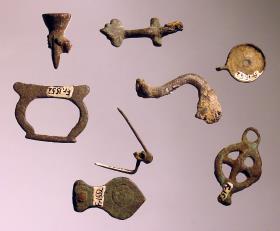 Neun verschiedene Teile: Hand mit Fackel, Mithrassymbol (?) in Form einer Säge, Teil einer Siegelkapsel, Miniaturhenkel, Fibelfragmente etc.