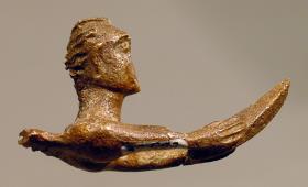 Vorderteil einer Figur, die in den ausgestreckten Händen ein unbestimmbares Gerät hält, hinten ein durchbohrter Zapfen