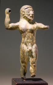 Archaische Statuette eines nackten Mannes, der mit der R. den Speer schwang. Linker Arm vorgestreckt, unten abgebrochen, ebenso die Beine