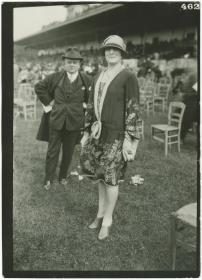 Frau in Ensemble und Mann in Anzug und Mantel auf dem Rennplatz in Chantilly